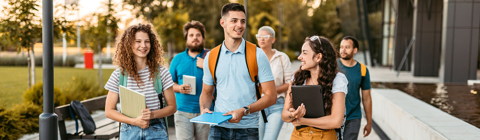 Group of friends walking on the university campus, holding books and notebooks.
