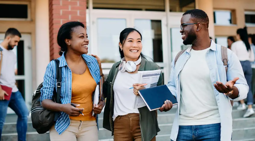 a group of diverse young adults holding notebooks outside of a classroom